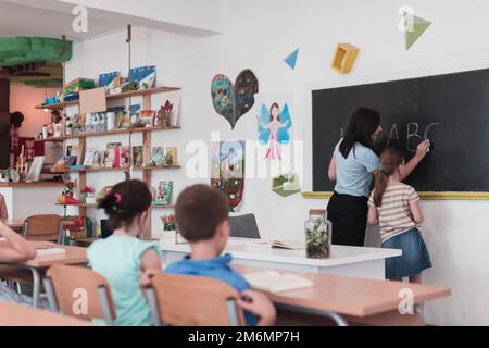 École primaire. L'enseignante aidant l'enfant étudiant tout en écrivant la réponse sur le tableau de surveillance. Banque D'Images