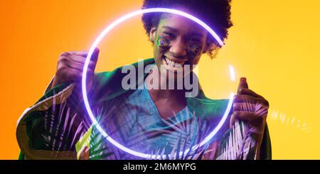 Afro-américaine heureuse femme fan avec drapeau brésilien et visage peint par cercle et plantes Banque D'Images