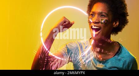 Fan afro-américain avec le visage du drapeau brésilien peint criant par le cercle et les plantes Banque D'Images