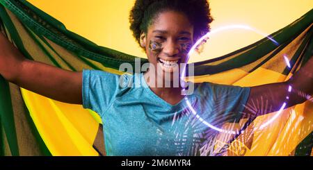 Joyeux fan afro-américain avec drapeau brésilien et visage peint par cercle et plantes Banque D'Images