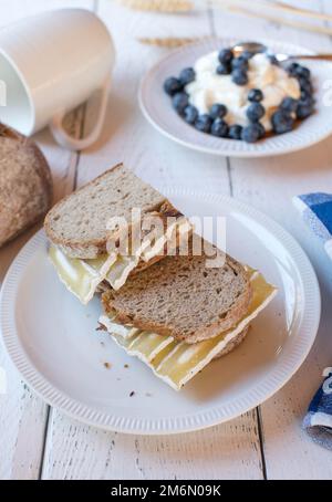 Sandwich-déjeuner sain avec pain au levain et fromage blanc. Servi avec un yaourt frais et des baies sur fond blanc Banque D'Images