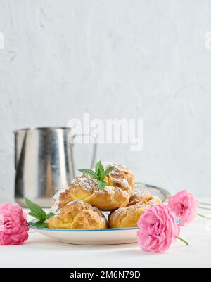 Eclairs cuits à la crème anglaise sur une plaque ronde en métal parsemée de sucre en poudre Banque D'Images