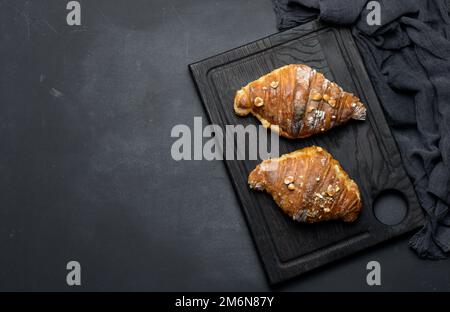 Croissant cuit sur une planche et arrosé de sucre en poudre, table noire. Pâtisseries appétissantes pour le petit déjeuner Banque D'Images