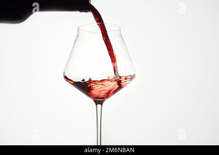 Le vin rouge est versé de la bouteille dans un verre transparent. Banque D'Images