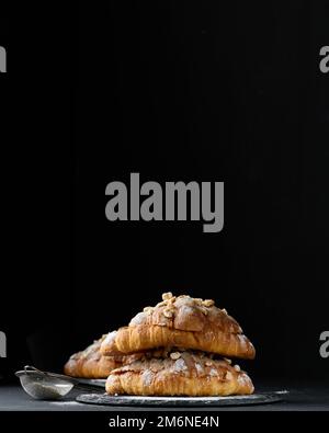 Croissant cuit sur une planche et arrosé de sucre en poudre, table noire. Pâtisseries appétissantes pour le petit déjeuner Banque D'Images