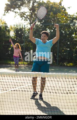 Couple biracial souriant jouant au tennis acclamations sur un court de tennis extérieur ensoleillé Banque D'Images