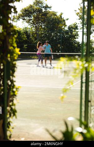 Couple biracial souriant jouant au tennis sur un court de tennis extérieur ensoleillé Banque D'Images