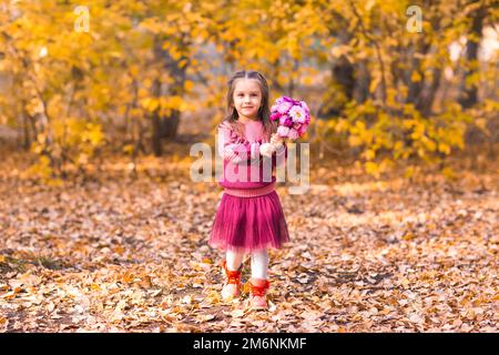 Jolie petite fille dans le parc d'automne avec bouquet de fleurs roses Banque D'Images