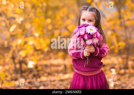 Jolie petite fille dans le parc d'automne avec bouquet de fleurs roses Banque D'Images