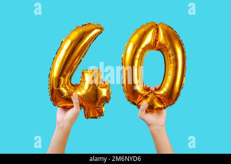 l'homme tient deux ballons en forme de nombre doré formant le numéro 40 sur un fond bleu Banque D'Images