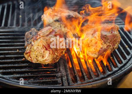 Traditionnel barbecue jarret d'agneau grillé comme gros plan sur un grill au charbon de bois avec feu et fumée Banque D'Images