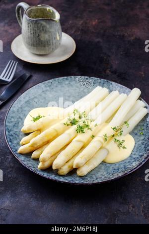 Asperges traditionnelles blanches vapeur de style moderne avec sauce au beurre hollandaise et cresson servies en gros plan sur un dessin nordique p Banque D'Images