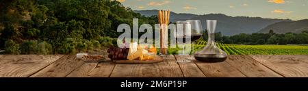 Décanter et deux verres avec délicieux vin rouge, vin de raisin et hors-d'œuvre au fromage debout sur une table en bois sur un magnifique paysage de nature des champs et Banque D'Images