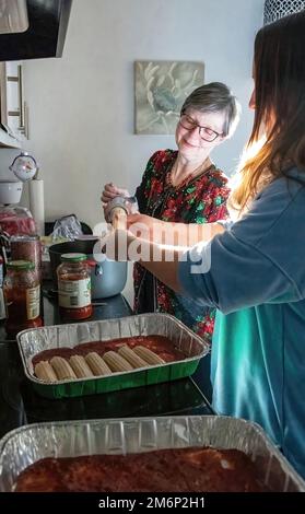 Deux femmes travaillent ensemble pour remplir les coquilles de pâtes de manucotti d'un mélange de fromage pour un plat de manucotti et de sauce marinara pour le dîner de la veille de Noël. Banque D'Images