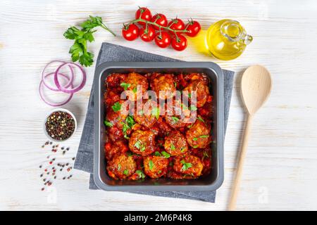 Boulettes de viande faites maison avec sauce tomate et épices servies dans une casserole noire sur fond de bois blanc. De savoureuses boulettes de viande cuites à base de bœuf haché et de nourriture Banque D'Images