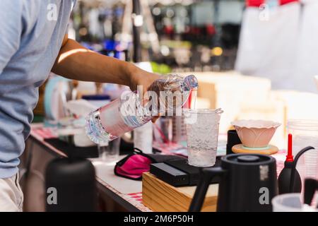 Le barista verse de l'eau à la main dans le verre en plastique avec du givre. Banque D'Images