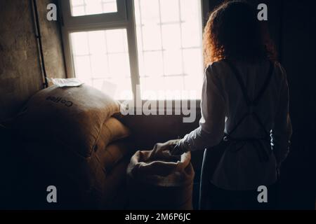 Grains de café verts dans un sac de toile de jute et un plat à rôtir femme avec une pelle Banque D'Images