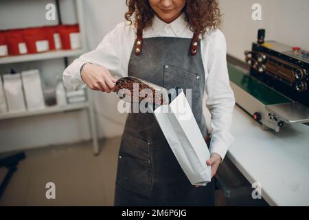 Grains de café frais torréfiés jeune femme emballant la machine dans un sac scellé sous vide Banque D'Images