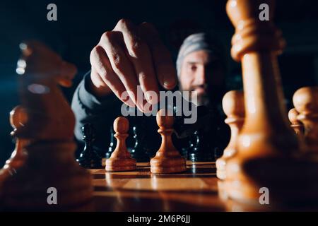 Jeune adulte beau homme jouant aux échecs dans l'obscurité avec le côté éclairé Banque D'Images