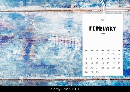 Février 2023 page calendrier pendu avec corde blanche sur fond de bois bleu ancien. Banque D'Images