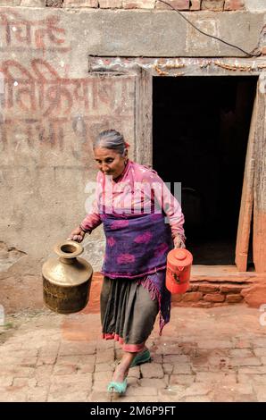 Visages du Népal : une femme âgée porte un bol d'eau Banque D'Images