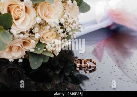 Une belle image aux tons avec des anneaux de mariage se trouve sur une surface noire sur le fond d'un bouquet de fleurs Banque D'Images