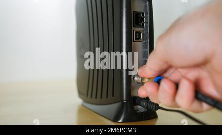 Connexion du câble coaxial au modem câble. Homme installant un accès Internet haut débit. Banque D'Images