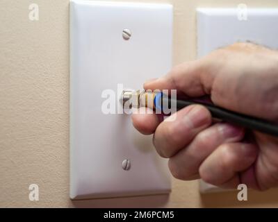 Électricien mâle reliant le câble coaxial à la prise murale. Connexion filaire coaxiale pour téléviseur et Internet haut débit. Installation du service de télévision. Banque D'Images