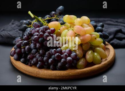 Raisins noirs et verts dans une plaque ronde en bois sur une table noire Banque D'Images