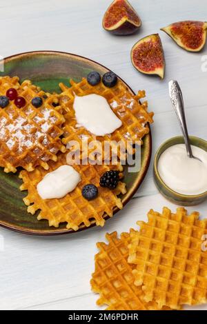 Yaourt dans un bol, gaufres et figues sur la table. Gaufres avec yaourt et baies sur une assiette verte. Vue de dessus. Arrière-plan blanc. Banque D'Images