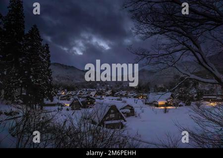 Lumières des maisons dans le village agricole traditionnel dans la vallée enneigée au crépuscule Banque D'Images