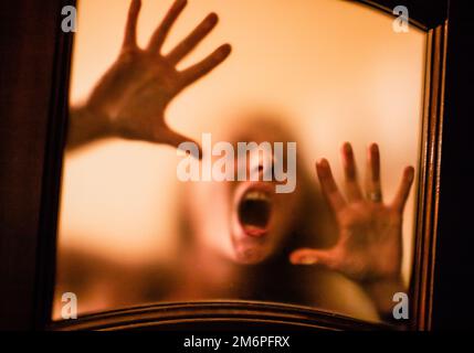Image effrayante des mains derrière le verre, femme fantôme d'horreur derrière la porte, concept d'Halloween Banque D'Images