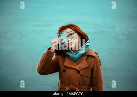 Portrait d'une belle femme asiatique aux cheveux rouges tenant un morceau de glace transparent dans ses mains et se tenant près de la mer froide un jour d'hiver. Un long Banque D'Images