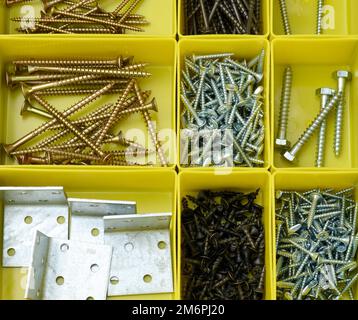 Diverses vis métalliques dans des récipients en plastique jaune séparés. Banque D'Images