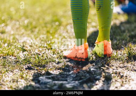 Jambes du joueur de football debout sur terrain boueux. Vêtements de football recouverts de boue. Match de football de niveau junior le jour de la pluie Banque D'Images