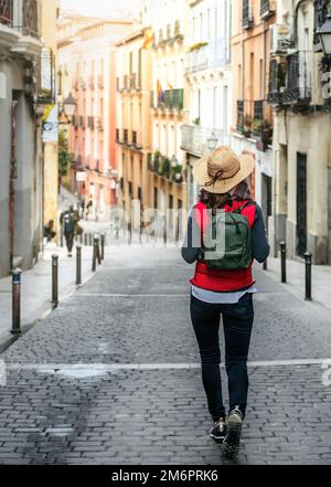 Une touriste femelle, dos tourné, portant un chapeau et un sac à dos, descend une rue dans le centre historique de Madrid. Tourisme de randonnée en Espagne. Banque D'Images