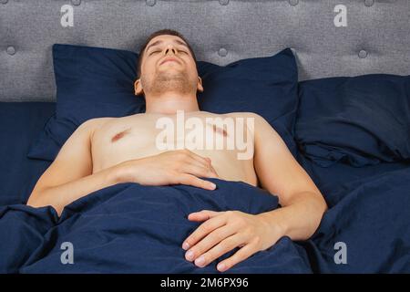 Beau jeune homme dormant confortablement sur le lit la nuit dans sa chambre sans vêtements. Chambre Bachelor. Sommeil profond. Banque D'Images