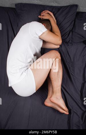 Beau jeune homme dormant confortablement sur le lit la nuit dans sa chambre portant un pyjama. Chambre Bachelor. En position fœtale. Banque D'Images