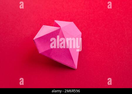 Coeur de papier rose origami isolé sur fond rouge Banque D'Images