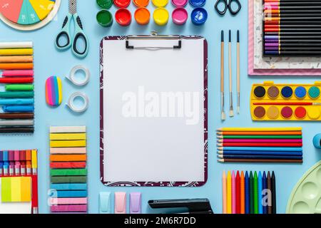 Fournitures scolaires colorées placées sur fond bleu avec du papier blanc ordinaire au milieu Banque D'Images