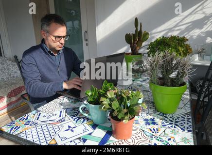 Homme travaillant de la maison dans des vêtements élégants et décontractés avec ordinateur portable à l'extérieur véranda avec des plantes vertes sur la table. Italie Banque D'Images