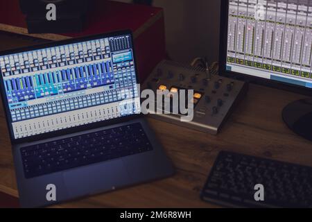 Gros plan allumé sur un ordinateur portable et écran de moniteur avec panneau de mixage sur une table dans un studio de diffusion et d'enregistrement sonore Banque D'Images