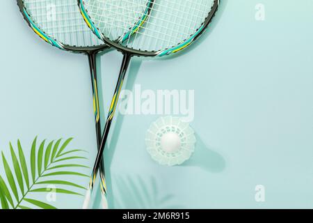 Badminton. Sports de compétition et tournoi de match avec raquettes de badminton et shuttlecock sur fond bleu avec feuilles de palmier et ombres. En bonne santé Banque D'Images