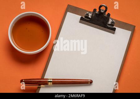 presse-papiers avec papier vierge, bureau plat avec une tasse de thé et un stylo élégant Banque D'Images