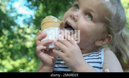 Une petite fille mignonne mange de la glace à l'extérieur. Portrait en gros plan d'une fille blonde assise sur le banc du parc et mangeant de la glace. Odessa, Ukraine Banque D'Images