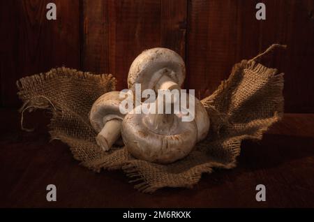 Champignons sur une serviette en toile de jute sur fond de bois sombre dans un style rustique Banque D'Images