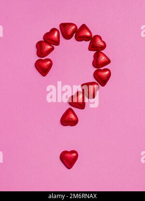 Être ma Saint-Valentin ? Plus grand signe de point d'interrogation fait de coeurs de chocolats rouges sur fond rose. Saint Valentin. Arrière-plan de vacances Banque D'Images