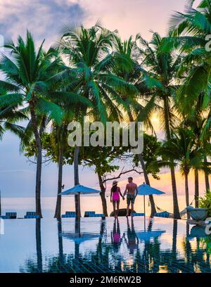 Couple d'hommes et de femmes se détendant près de la piscine dans les chaises de plage, piscine tropicale Banque D'Images