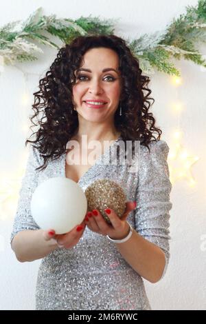 Bonne femme en robe de Noël étincelante avec maquillage festif et coiffure tenant des boules de Noël arbre Banque D'Images