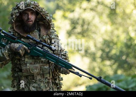 Un militaire ou un joueur d'aérosoft dans un costume de camouflage qui se faufile dans la rivière et vise d'un fusil de sniper sur le côté ou à la cible. Banque D'Images